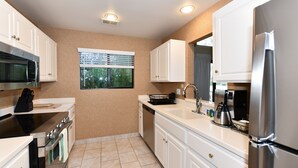 A modern kitchen with white cabinets, stainless steel appliances, and a window with blinds.
