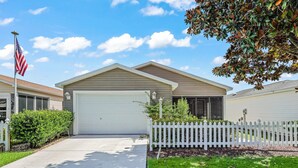 A single-story house with a white garage door, a small front yard with a white picket fence, and a well-maintained lawn.
