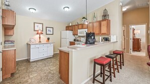 A kitchen with a central island, wooden cabinets, a microwave, and a refrigerator. There are bar stools and a ceiling light fixture.