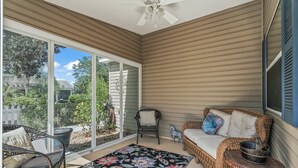 A sunlit patio with wicker furniture, a colorful rug, and a ceiling fan.