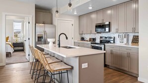 A modern kitchen with a central island, stainless steel appliances, and light wood cabinets. - Coco Dunes 2 Bedroom Condo (St. George)