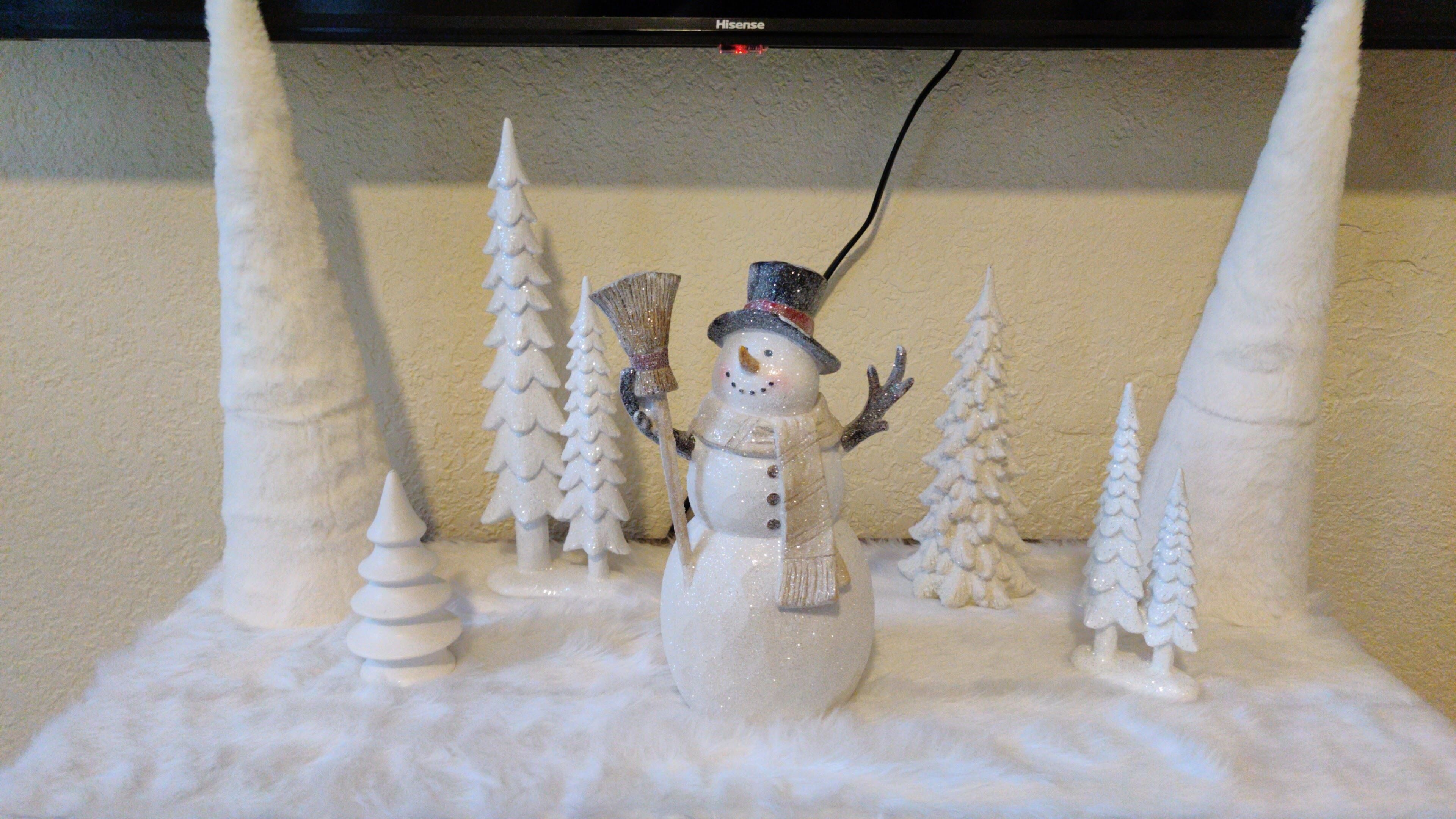 A snowman decoration with a broom and a hat, surrounded by snow-covered trees and a snow globe base.