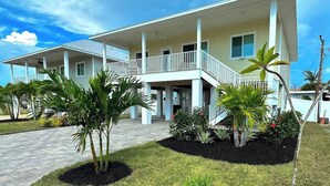 A two-story house with a balcony, surrounded by well-maintained lawn and tropical plants. - Beyond The Sea · 70+ 5-Star ·  Walk to Beach-Town (Fort Myers Beach)