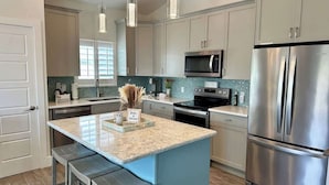 A modern kitchen with stainless steel appliances, a central island with bar stools, and pendant lighting. - Beyond The Sea · 70+ 5-Star ·  Walk to Beach-Town (Fort Myers Beach)