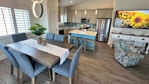 A modern kitchen with stainless steel appliances, a dining area with blue chairs, and a TV displaying a sunflower. - Beyond The Sea · 70+ 5-Star ·  Walk to Beach-Town (Fort Myers Beach)