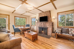 A cozy living room with a stone fireplace, wooden furniture, and large windows offering a view of the outdoors. - Kittery West - Monthly Long-term Vacation Rental Only 2 Bedroom Home by RedAwning (Estes Park)