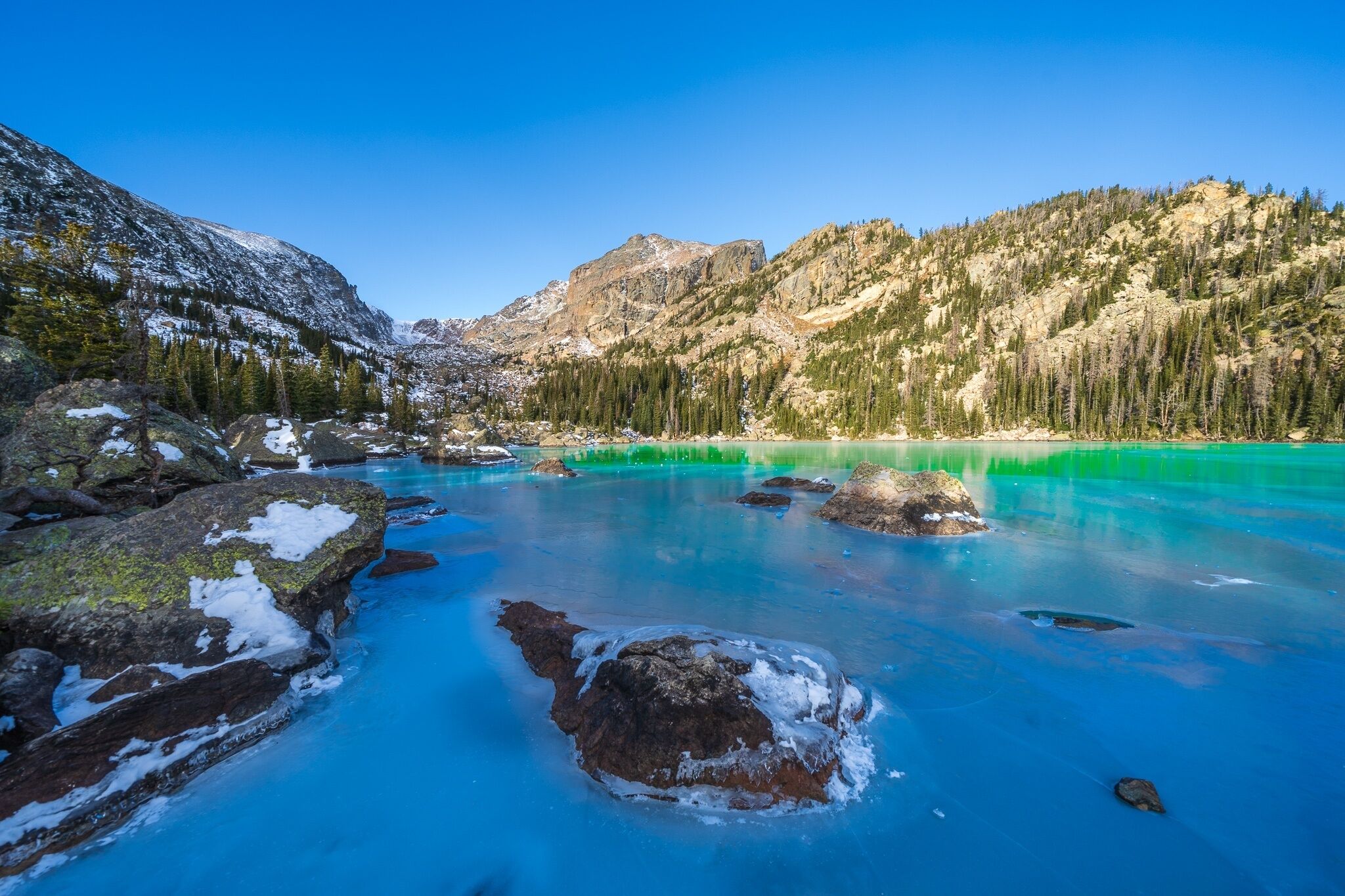 A clear, turquoise lake surrounded by snow-covered mountains and dense forests.
