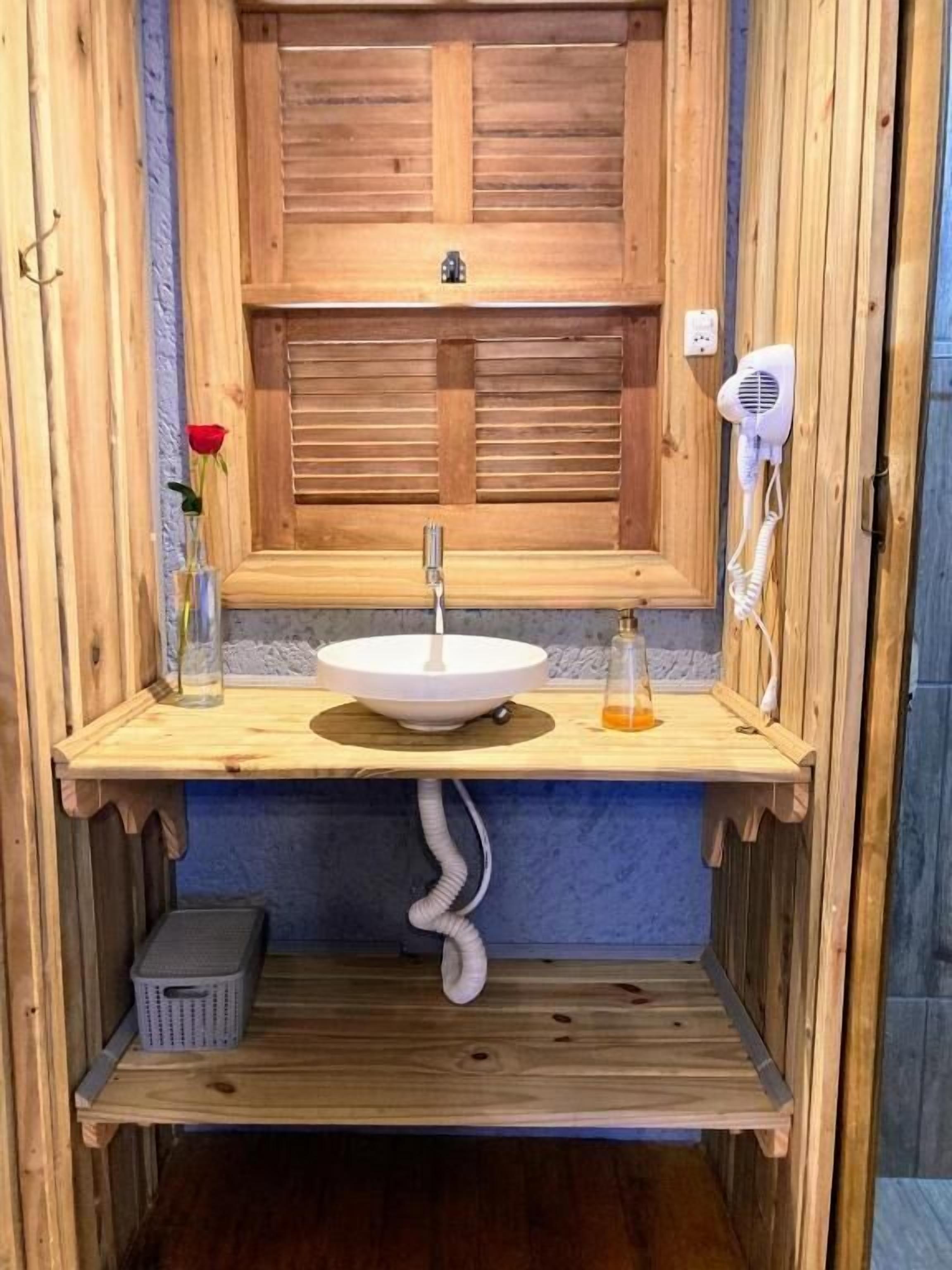 A wooden bathroom with a white sink, a hairdryer, and a vase with a red rose.
