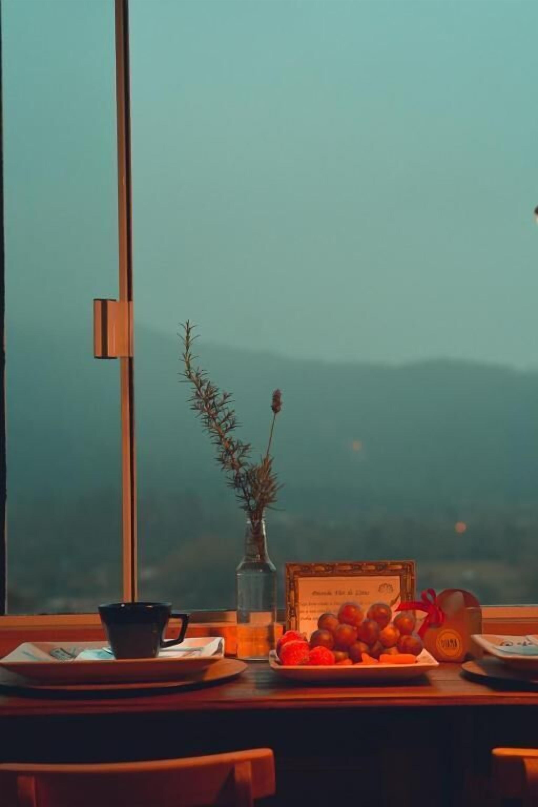 Uma mesa com uma travessa de fruta, uma chávena, um vaso com uma planta e um certificado emoldurado.