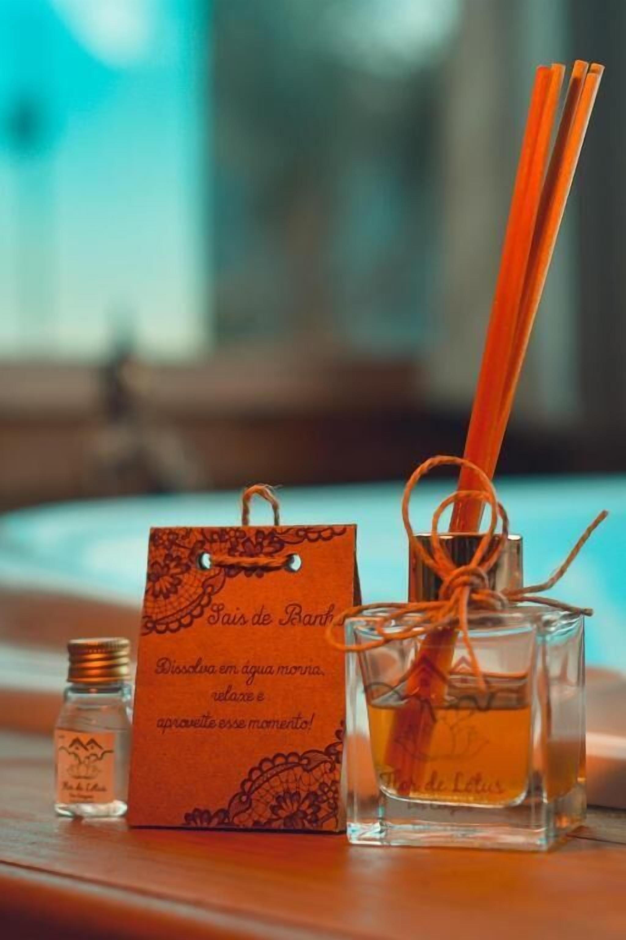 Una botella de vidrio pequeña con etiqueta, una caja cuadrada con texto y dos difusores de caña naranja sobre una superficie de madera.