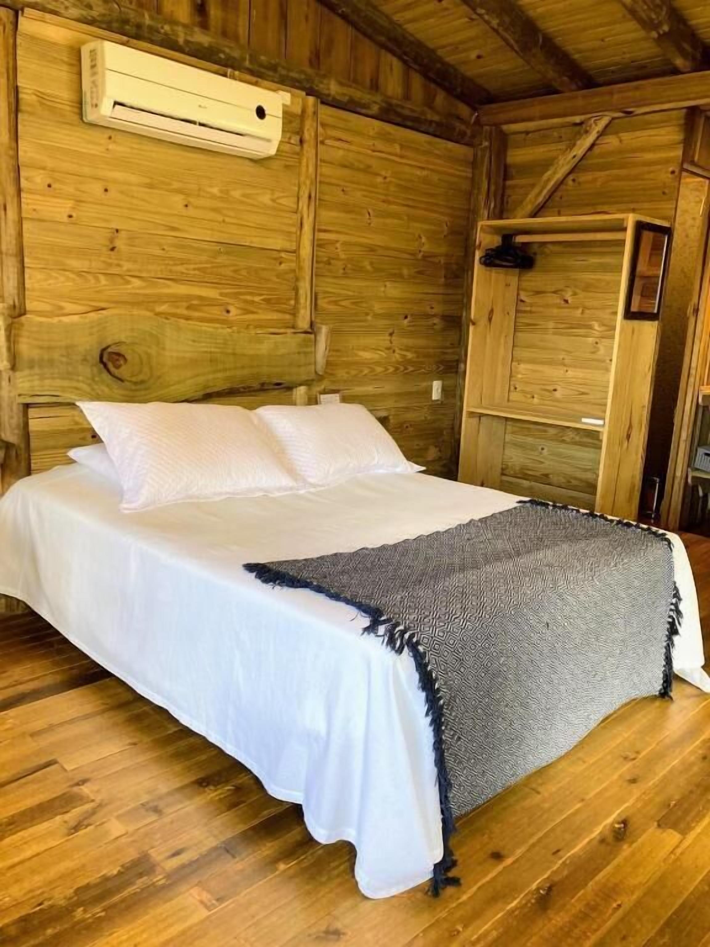Camera da letto in una baita di legno, con un letto, biancheria bianca e una coperta grigia.