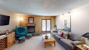 A cozy living room with a fireplace, a teal chair, a sofa, and a flat-screen TV.