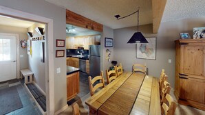 A modern kitchen with wooden cabinets, a stainless steel refrigerator, and a dining area with a long wooden table and chairs.