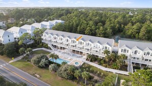 A multi-story hotel with a pool, surrounded by lush greenery and a clear sky.