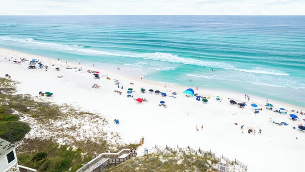 A beach with white sand, clear turquoise water, and umbrellas.