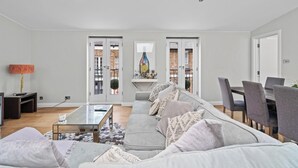 Un salon moderne avec un canapé gris, une table basse en verre et un coin repas avec des chaises grises.