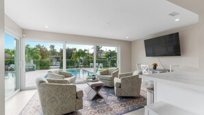 Un salon moderne avec vue sur la piscine, doté de sièges confortables et d’un téléviseur à écran plat.
