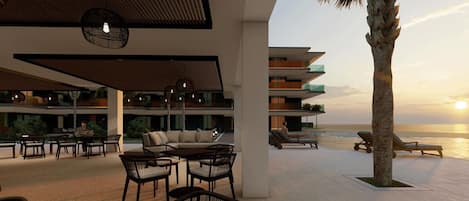 A modern resort with outdoor seating, a pool, and a view of the ocean at sunset.
