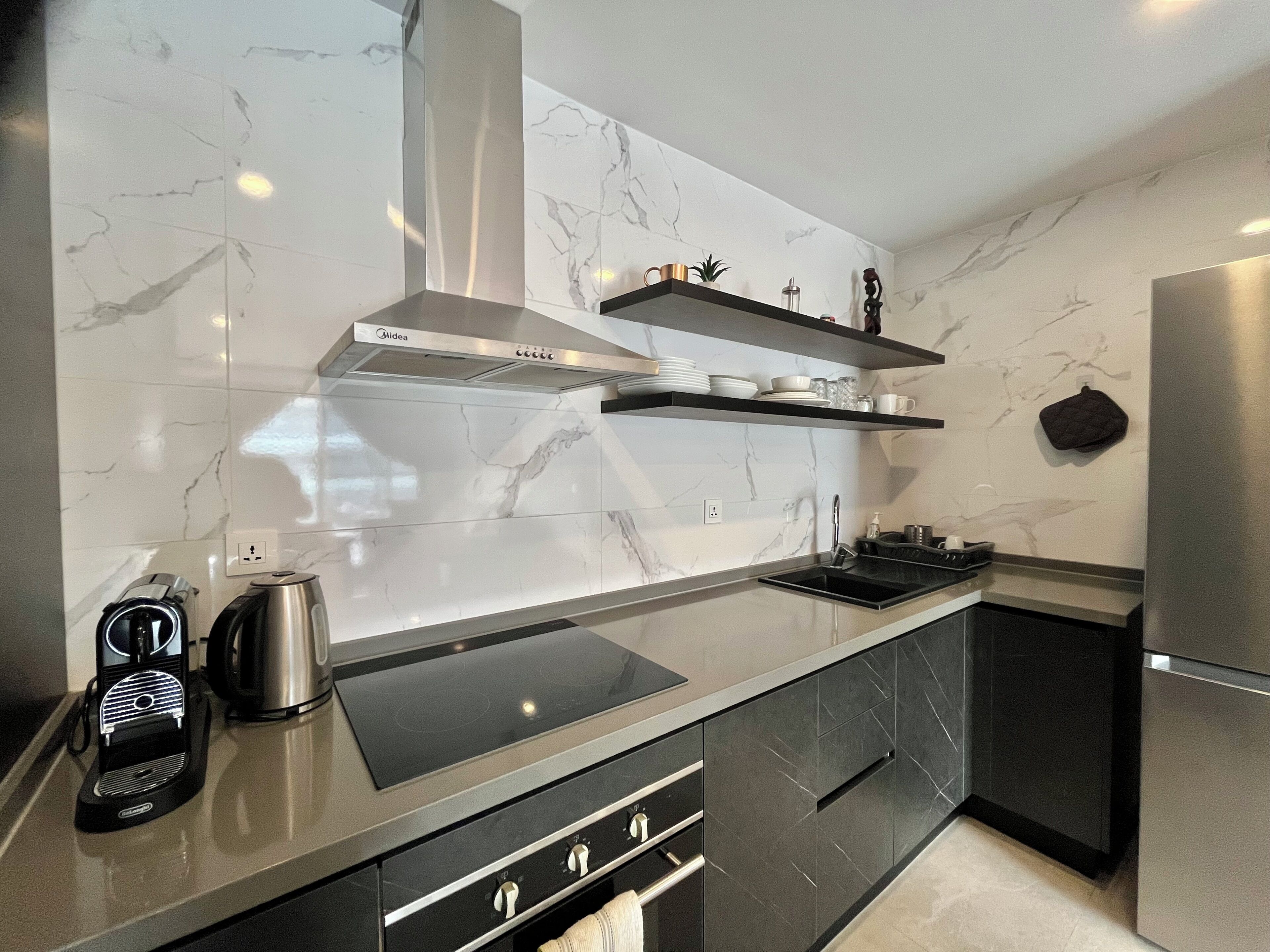 A modern kitchen with a sleek black countertop, stainless steel appliances, and marble backsplash.