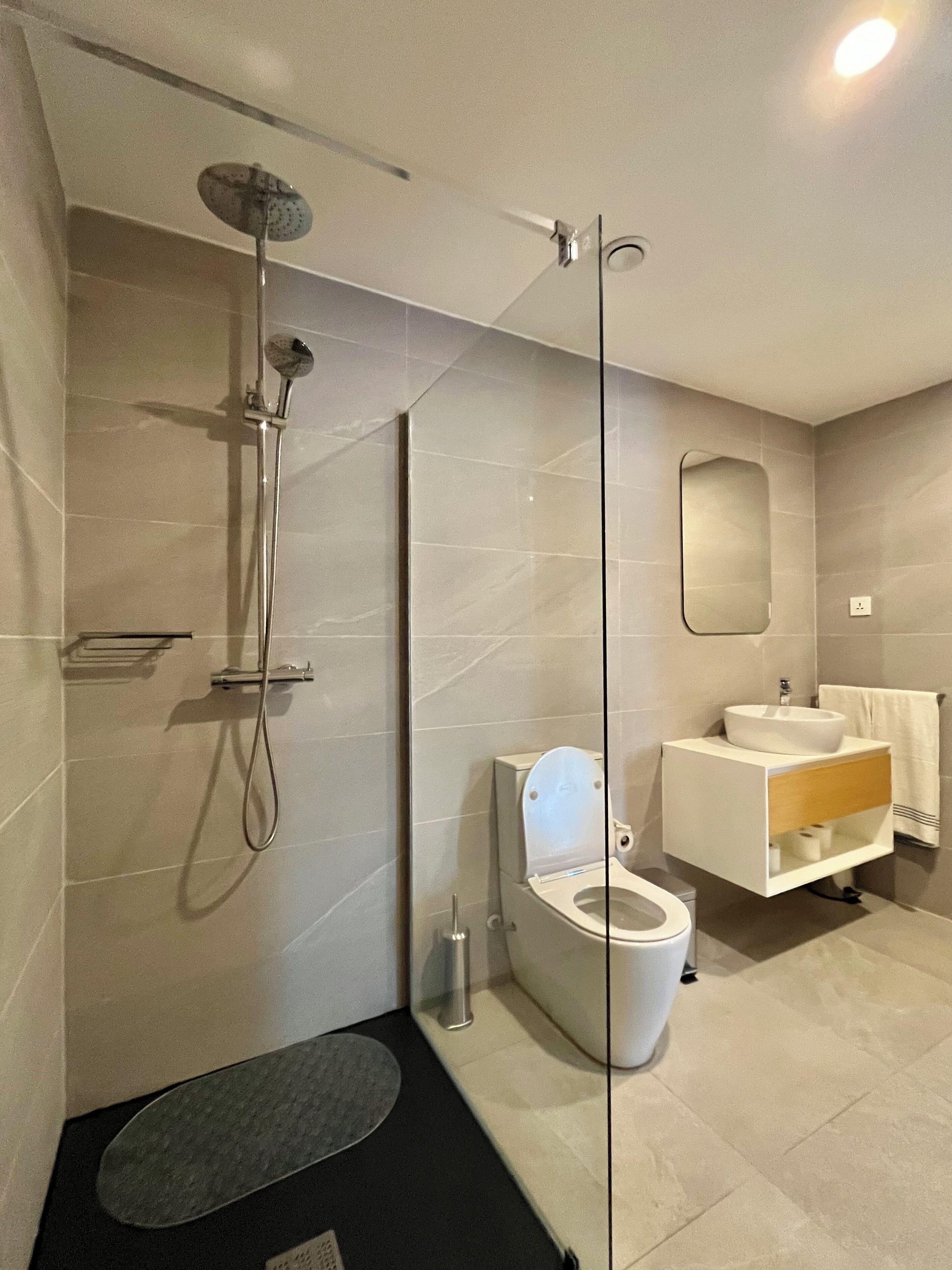 Un baño moderno con ducha de vidrio, inodoro y tocador con espejo.