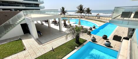 A modern hotel with a rooftop pool, outdoor seating, and a view of the ocean.