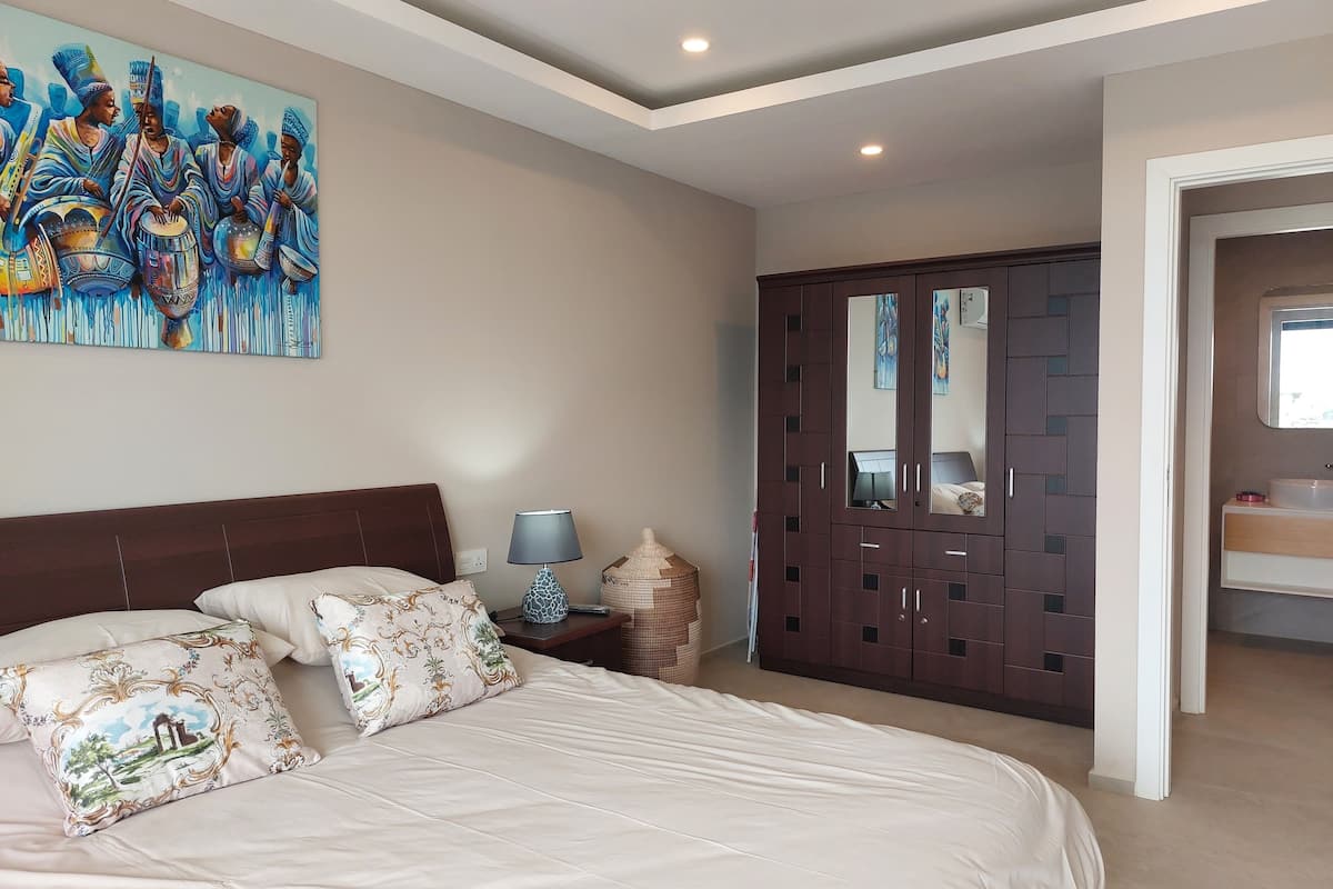 Un dormitorio con una cama grande, una mesita de noche, una lámpara, un armario y un cuadro en la pared.