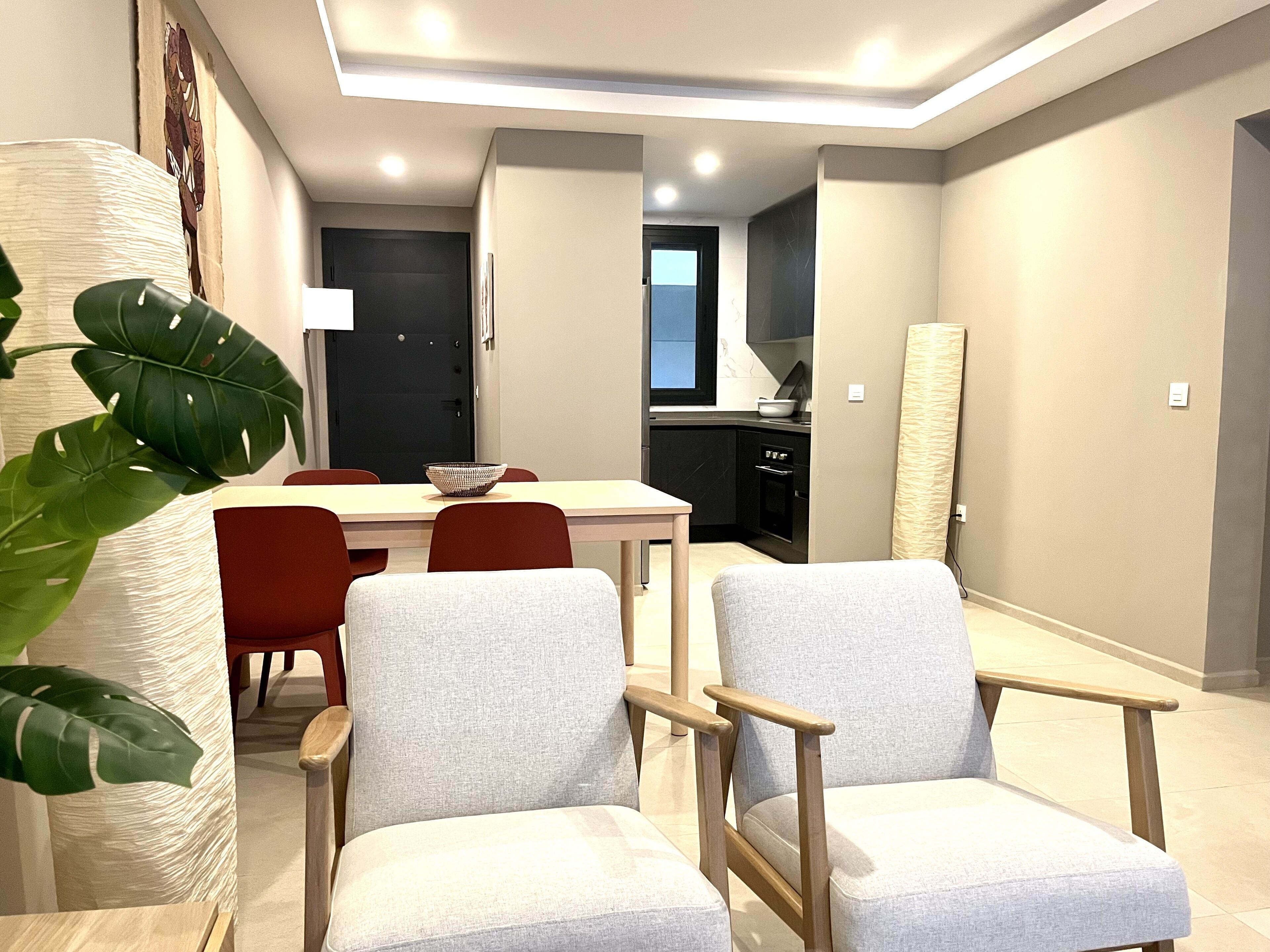 Un salon moderne comprenant un coin repas, une cuisine et une grande plante.