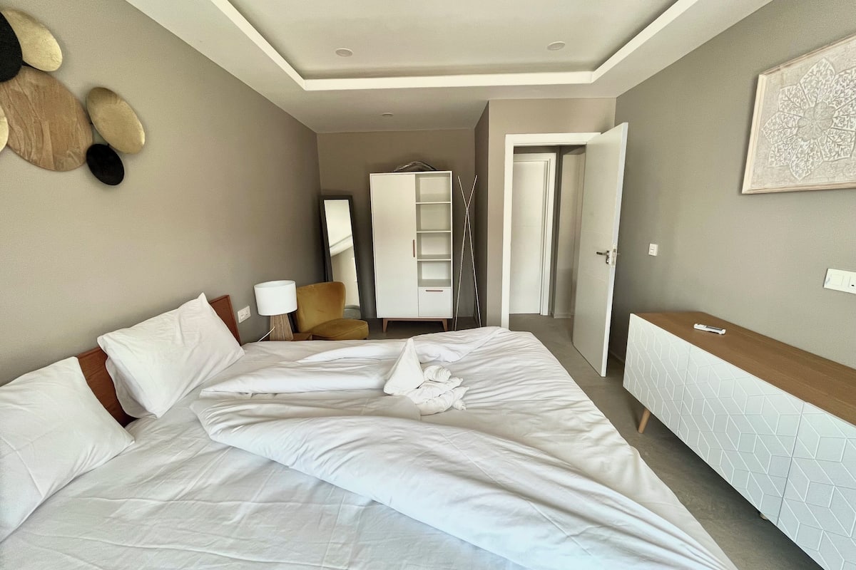 Una habitación de hotel con una cama grande, una mesita de noche, una silla, un armario y un espejo.
