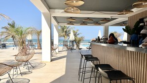 Un bar situé en bord de mer, avec des chaises en osier et une vue sur l’océan.