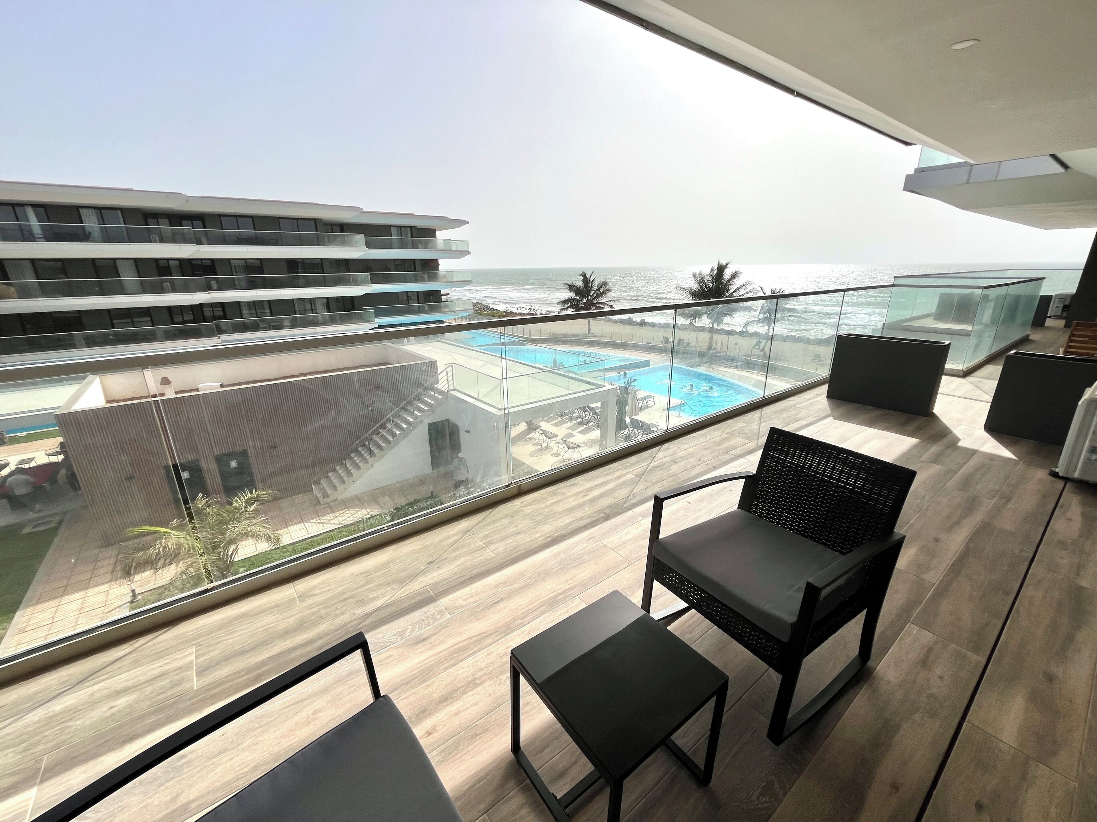 Un balcón con vista a la piscina, muebles modernos y una vista despejada del océano.