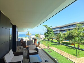 A balcony with a view of the sea, furnished with wicker chairs and a sofa, and a glass railing. - Kololi Sands (Serrekunda)