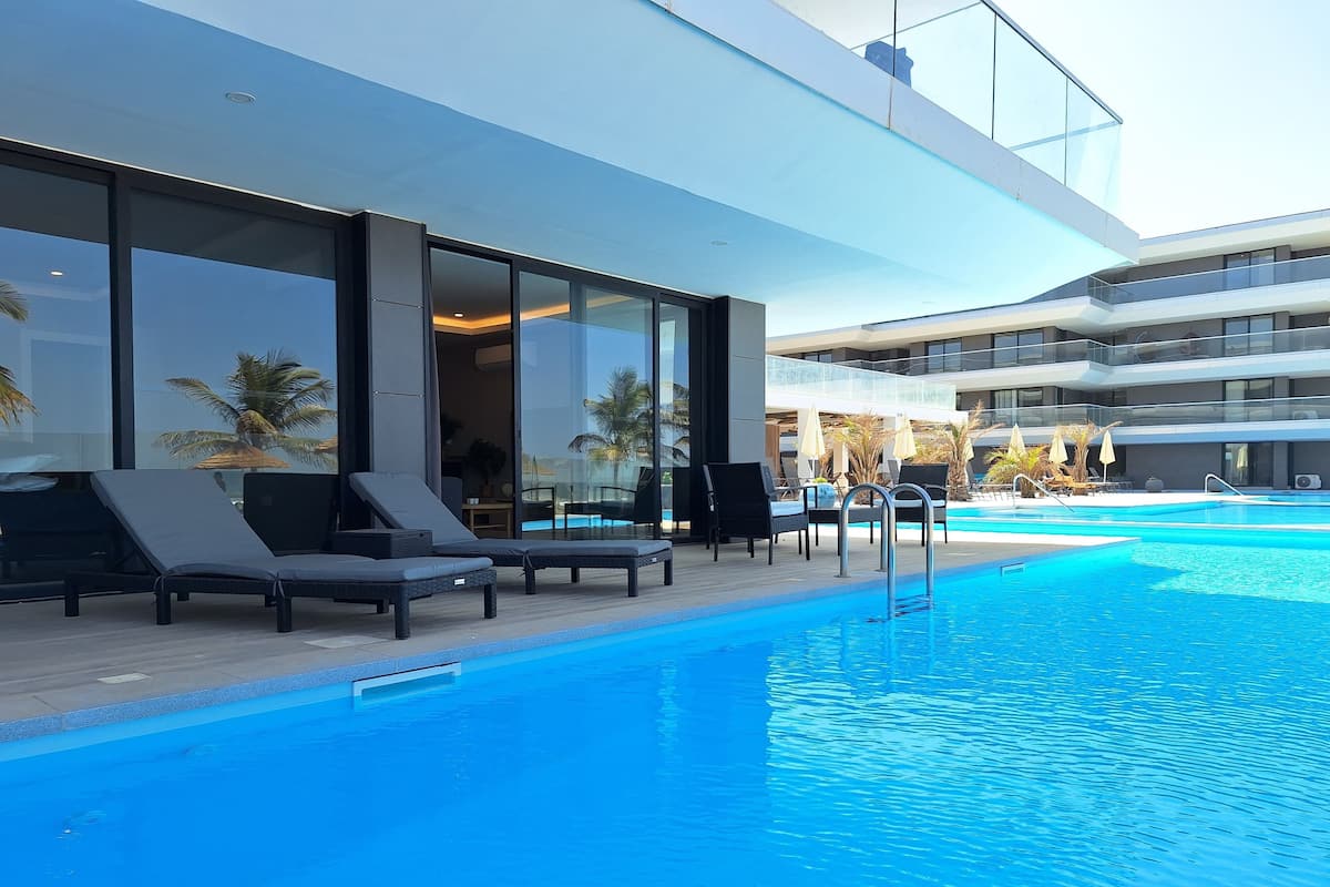 Un hotel moderno con piscina, tumbonas y una zona de balcón con paredes de cristal.