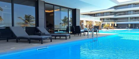 A modern hotel with a swimming pool, sun loungers, and a glass-enclosed balcony area.