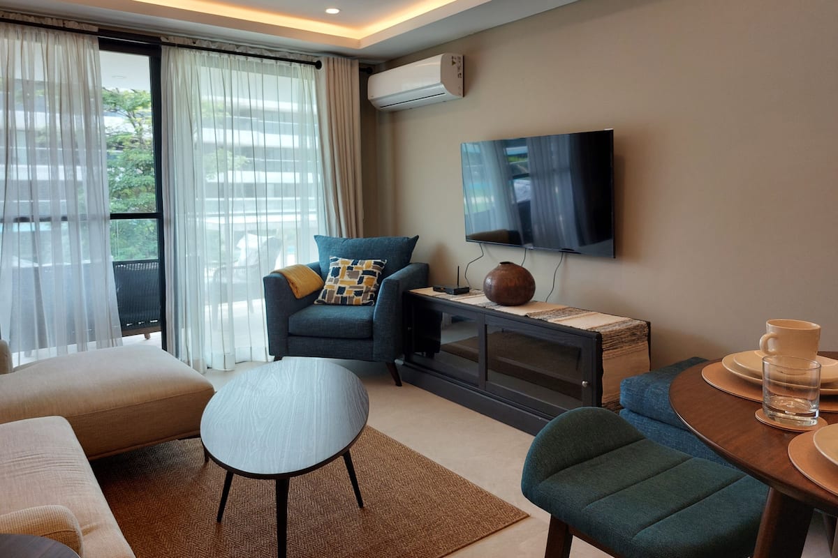 Una sala de estar moderna con sofá, sillón, mesa de centro y televisor montado en la pared.