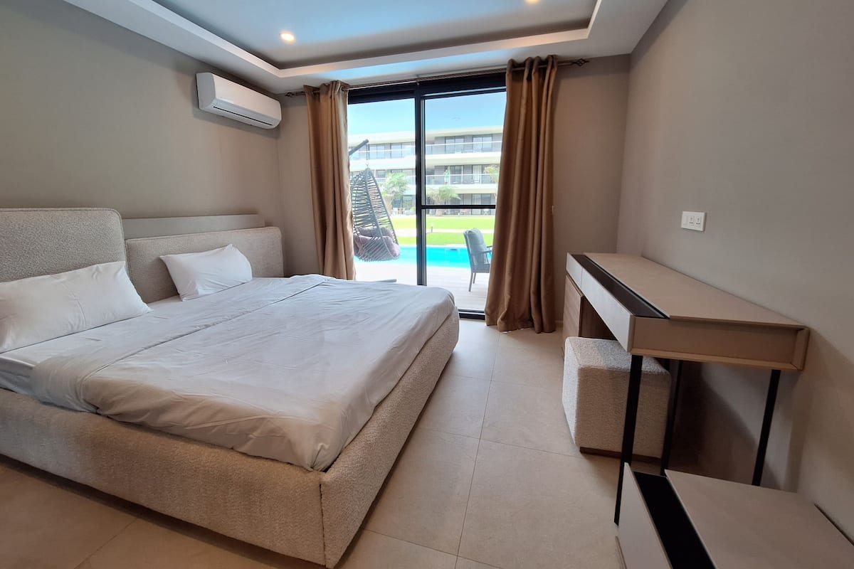 Una habitación de hotel moderna con una cama grande, un escritorio y vistas a una piscina y un edificio.