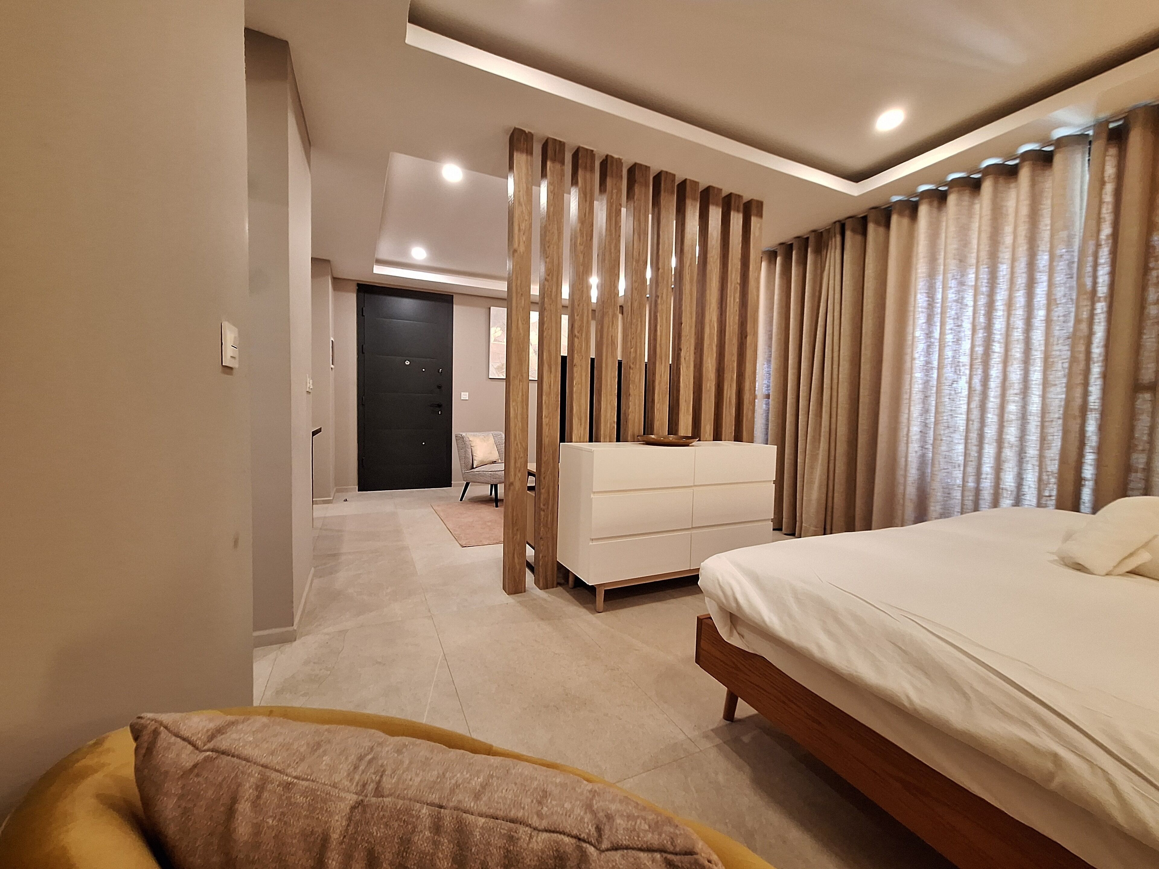 Une chambre moderne avec un grand lit, une commode blanche et un coin salon comprenant une chaise et une petite table.