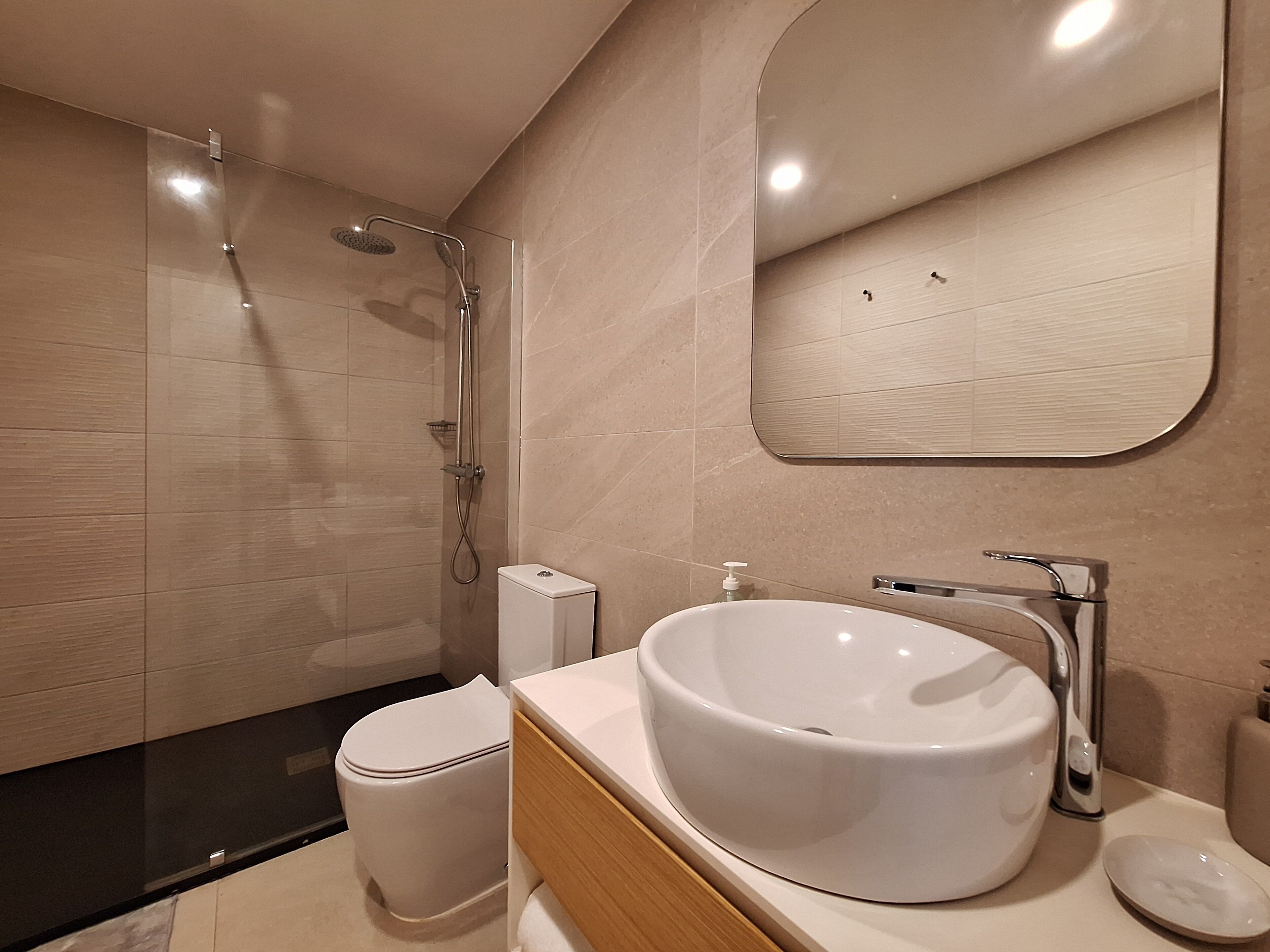 A modern bathroom with a glass-enclosed shower, a white toilet, and a large white sink with a mirror above it.