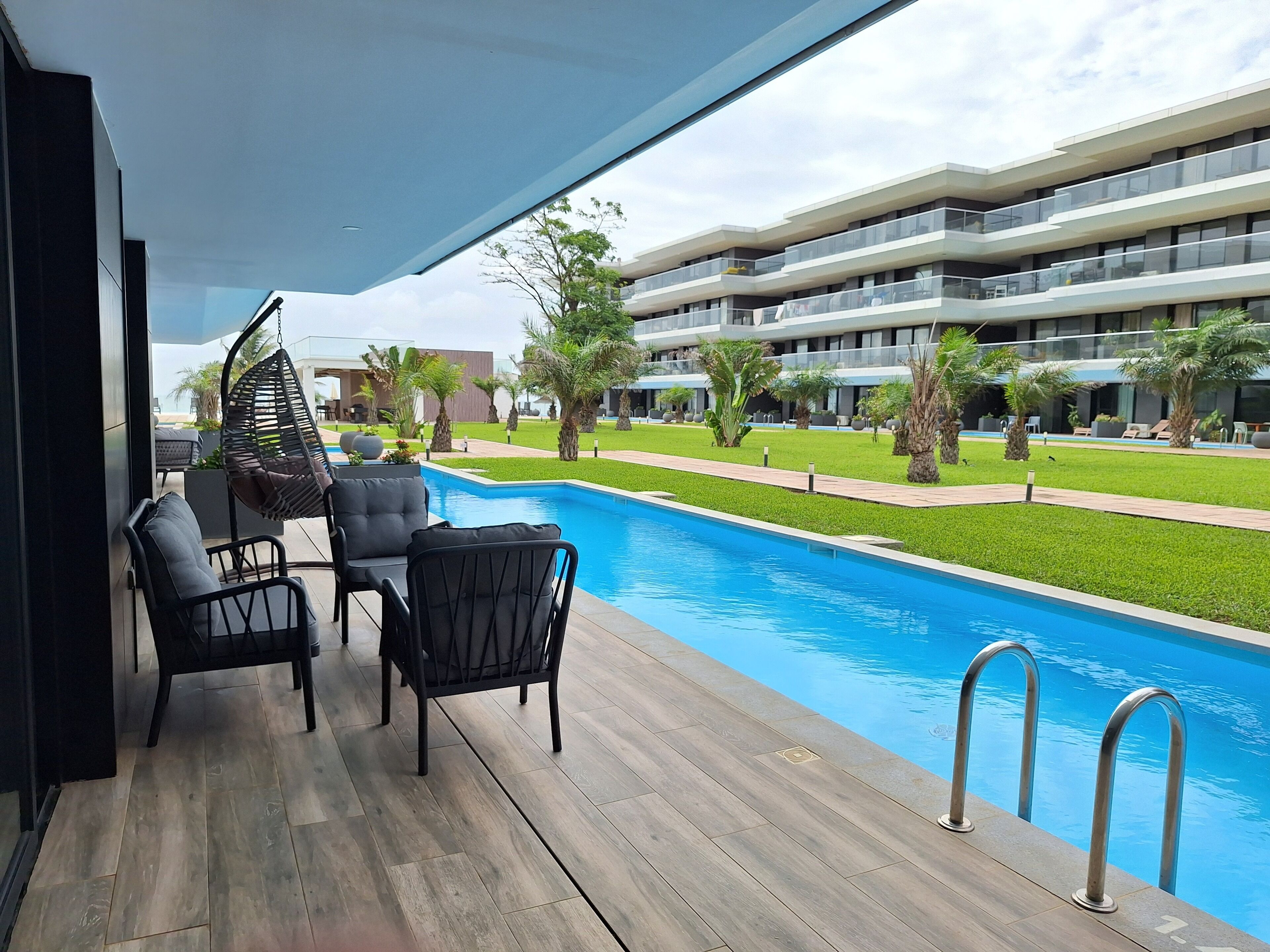 Zona junto a la piscina con un deck de madera, sillas negras y una silla colgante.