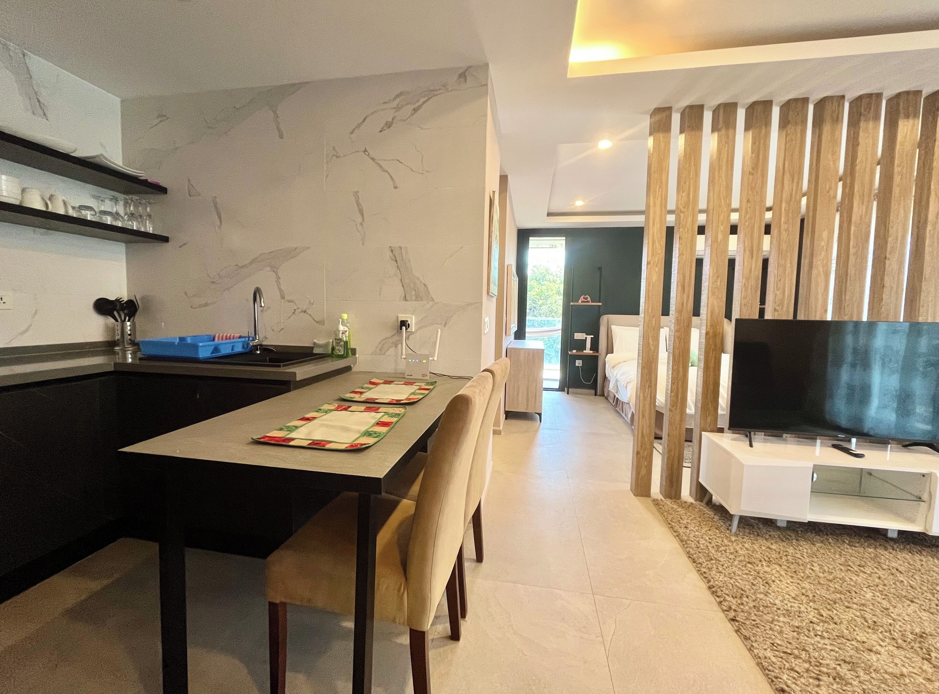 Een moderne keuken met een marmeren achterwand, een eethoek met tafel en stoelen, een televisie op een standaard, en een zithoek met een bank en gordijnen.