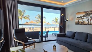 Une chambre d’hôtel moderne avec un balcon donnant sur une plage, un canapé, une table ronde et un tableau au mur.