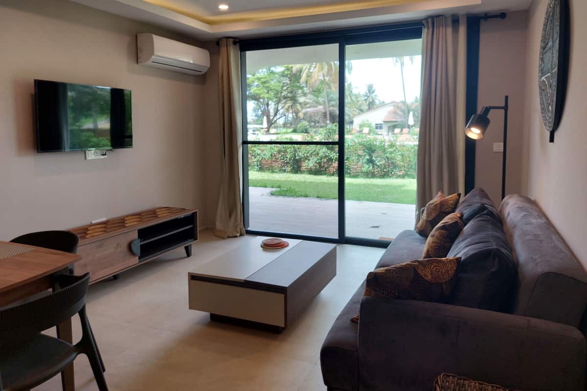 Una sala de estar moderna con un televisor de pantalla plana, un sofá, una mesa de centro y una zona de comedor con una mesa y sillas de madera.