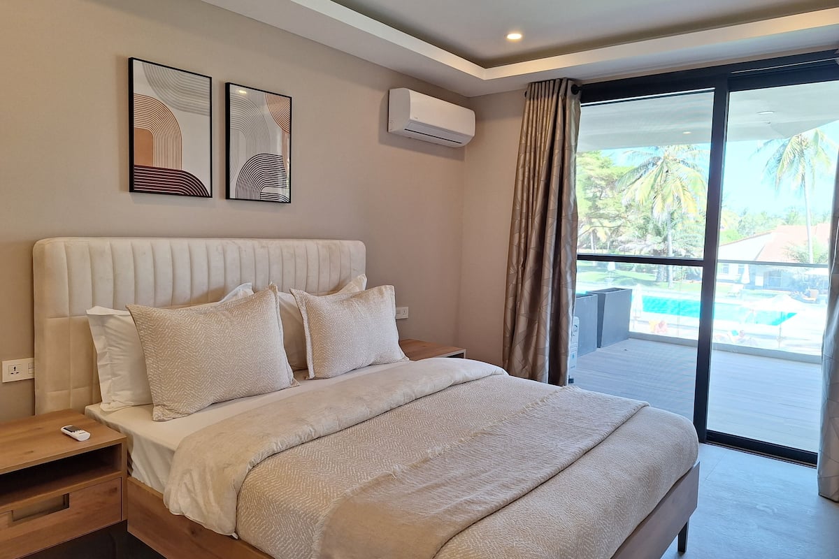 Un dormitorio moderno con una cama grande, una mesita de noche, aire acondicionado montado en la pared y vistas a una piscina a través de una puerta corrediza de vidrio.