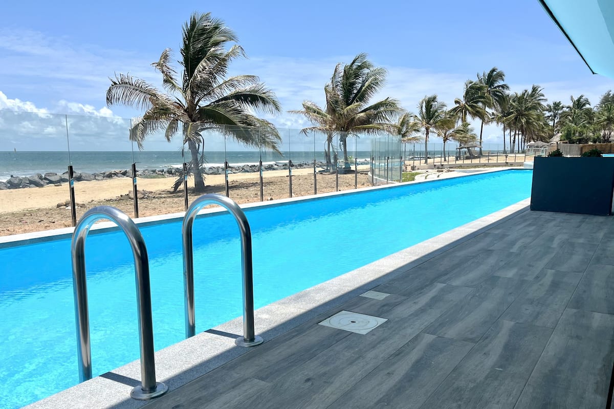 Una piscina con vistas a la playa y palmeras.