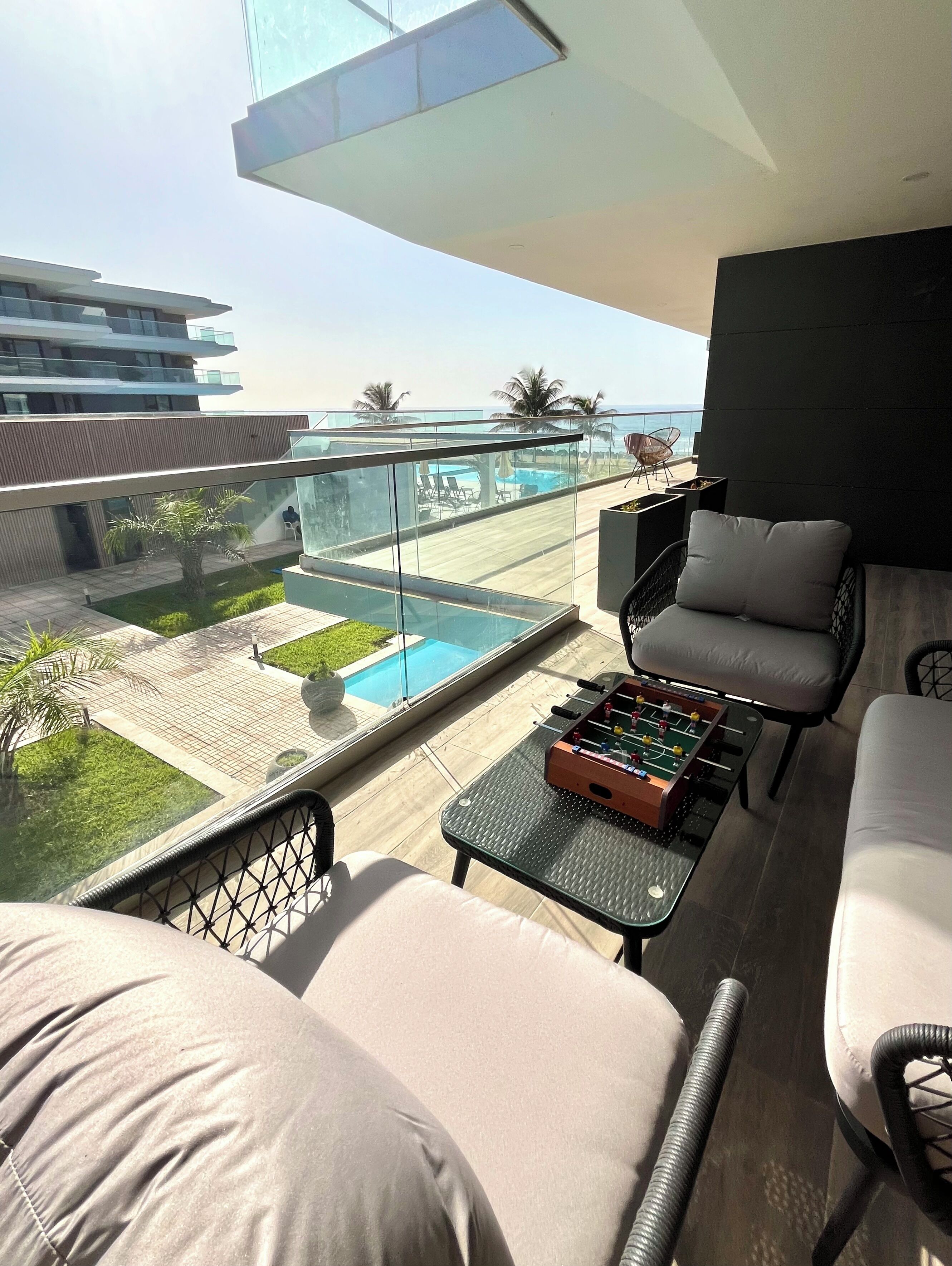 A balcony with a glass railing, a pool, and outdoor seating.