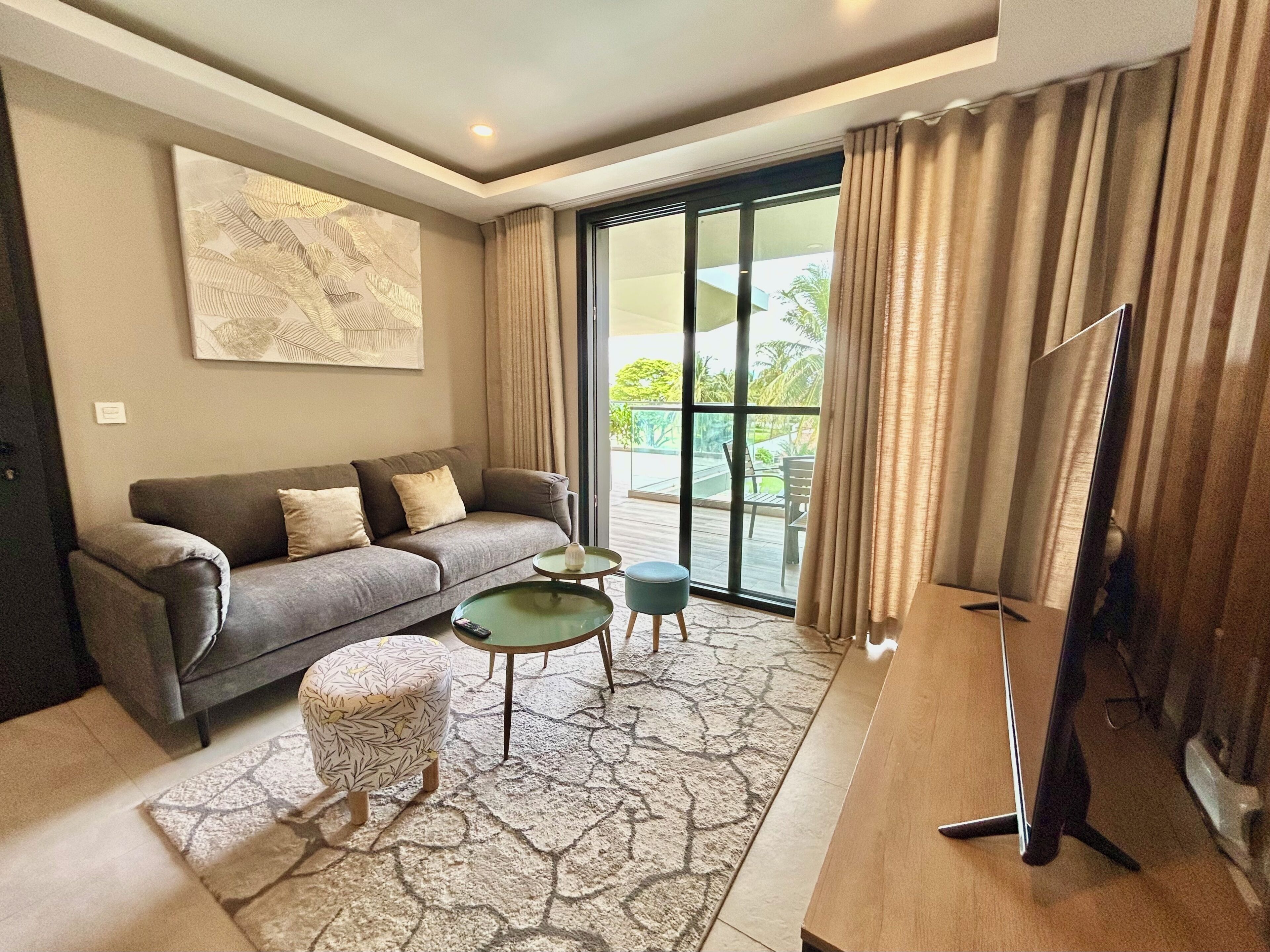A modern living room with a sofa, ottoman, coffee table, and a flat-screen TV.
