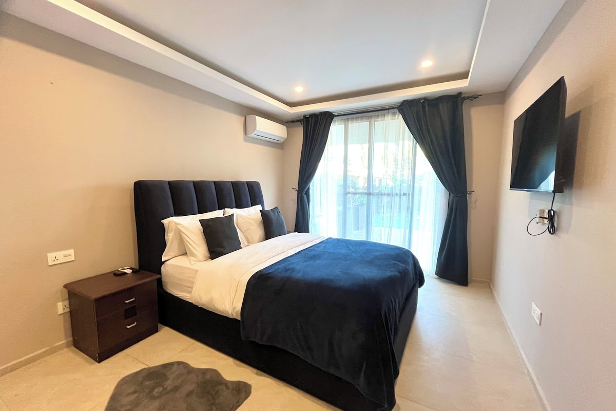 Un dormitorio moderno con una cama grande, una mesita de noche, un televisor y un equipo de aire acondicionado.