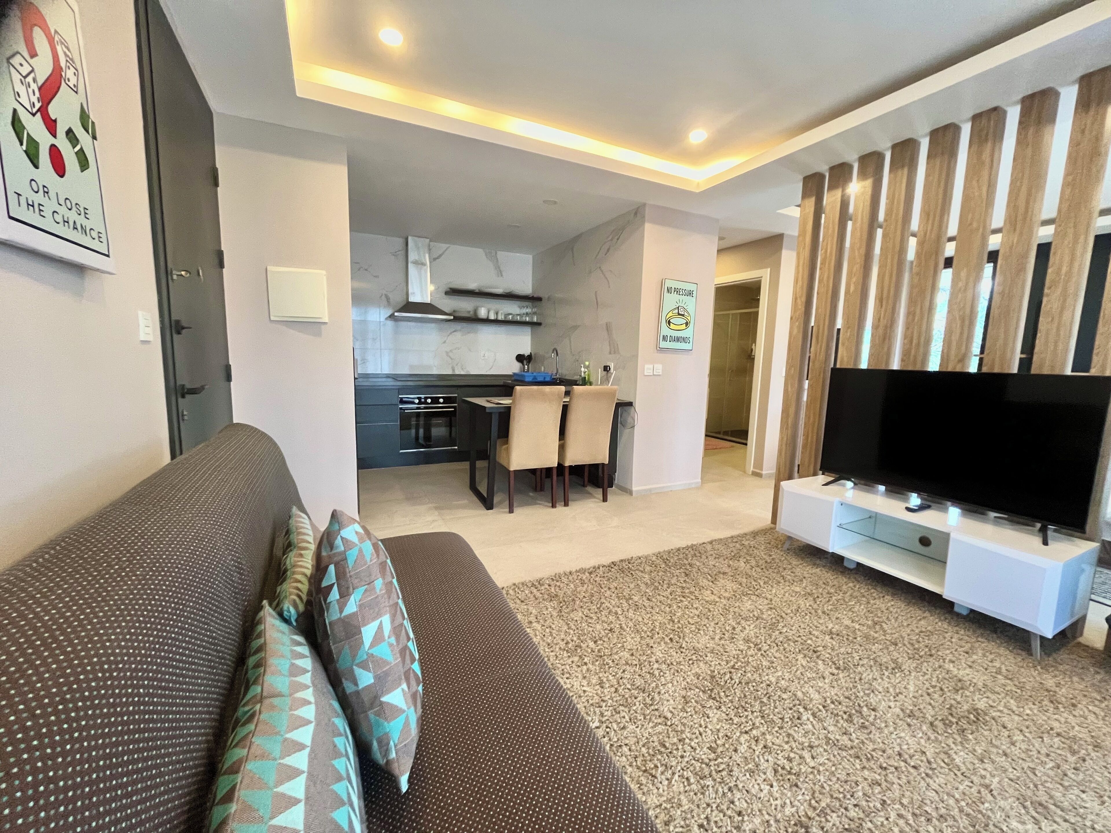 A modern living room with a sofa, a TV, and a kitchen in the background.