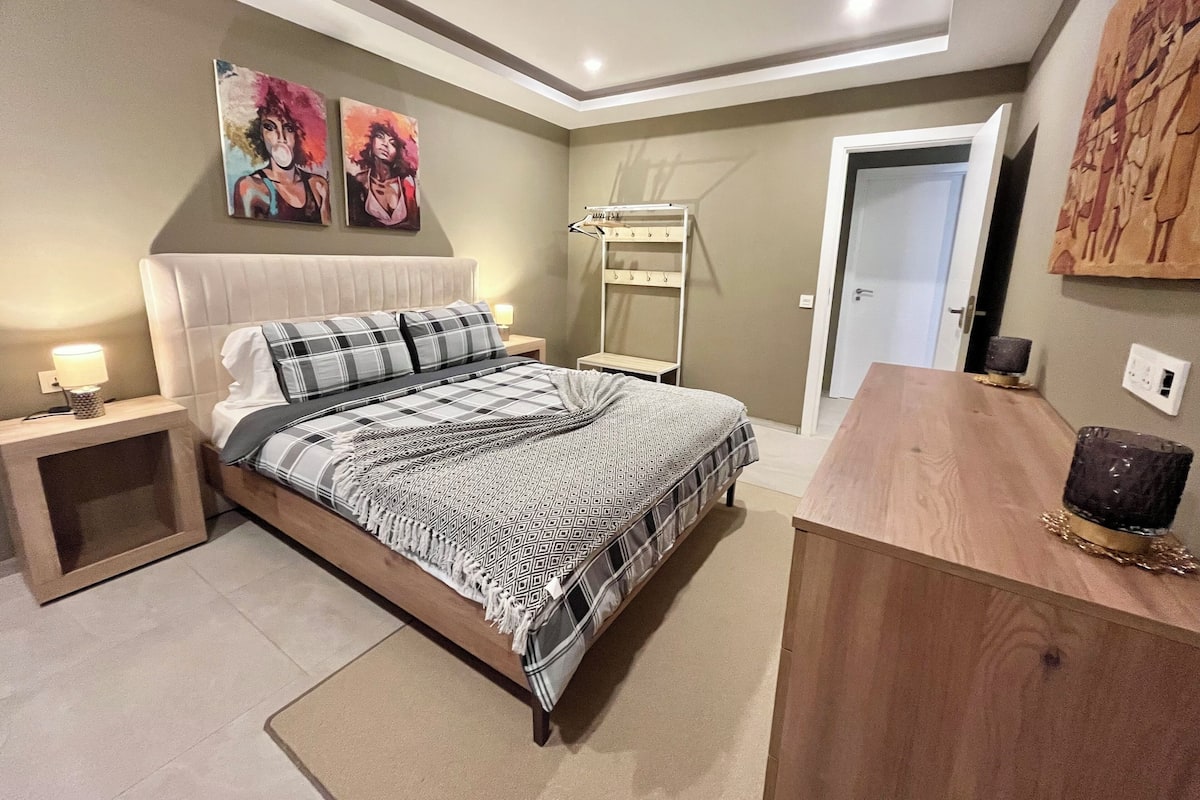 Un dormitorio con cama, mesitas de noche, cómoda y obras de arte en las paredes.