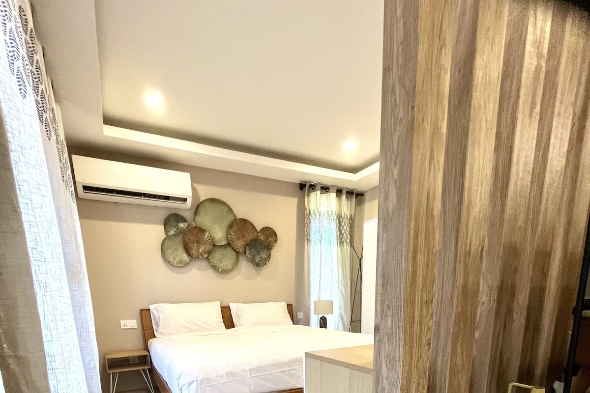 Un dormitorio moderno con cama, mesita de noche y un pequeño rincón de estar con taburetes.