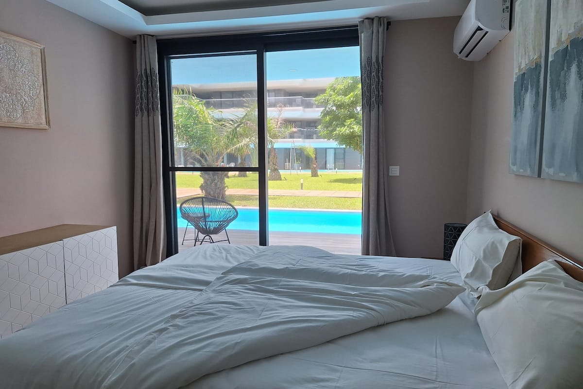 Habitación de hotel con una cama grande, vistas a una piscina y un equipo de aire acondicionado en la pared.
